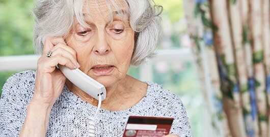 Rentnerin mit Telefonhörer und Kreditkarte in der Hand