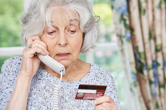 Rentnerin mit Telefonhörer und Kreditkarte in der Hand