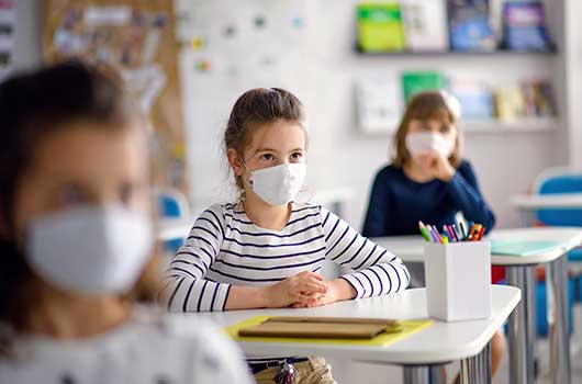 Kind mit Maske sitzt im Klassenzimmer - Arbeitsrecht