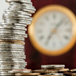 Geldmünzen und eine Uhr im Hintergrund - symbolisch für Zeit ist Geld