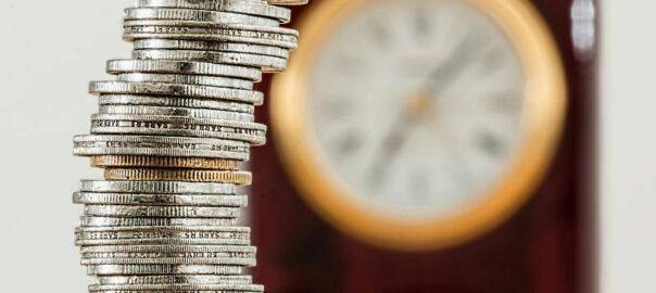 Geldmünzen und eine Uhr im Hintergrund - symbolisch für Zeit ist Geld