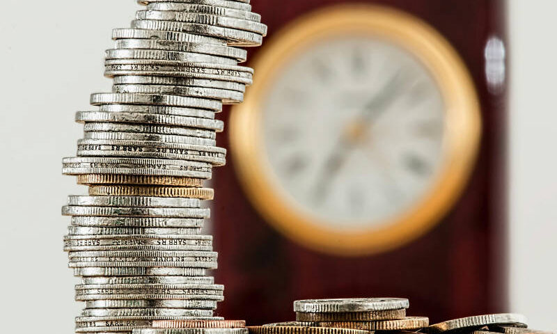 Geldmünzen und eine Uhr im Hintergrund - symbolisch für Zeit ist Geld