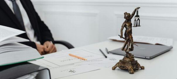 Schreibtisch mit Justitia-Figur, Akten und Laptop in einer Kanzlei, Symbolbild für ein Insolvenzverfahren.