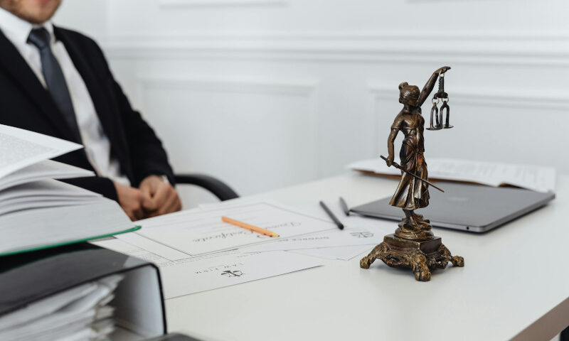 Schreibtisch mit Justitia-Figur, Akten und Laptop in einer Kanzlei, Symbolbild für ein Insolvenzverfahren.