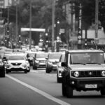 Dichter Stadtverkehr auf mehrspuriger Straße in Schwarzweiß, mit einem Suzuki Jimny im Vordergrund und weiteren PKW im Hintergrund.