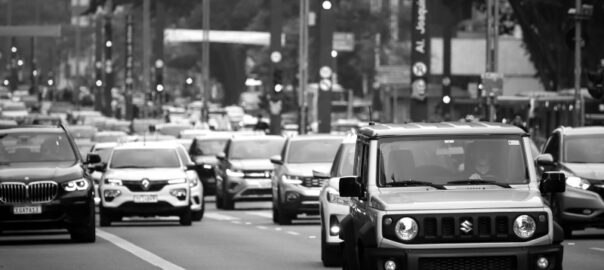 Dichter Stadtverkehr auf mehrspuriger Straße in Schwarzweiß, mit einem Suzuki Jimny im Vordergrund und weiteren PKW im Hintergrund.