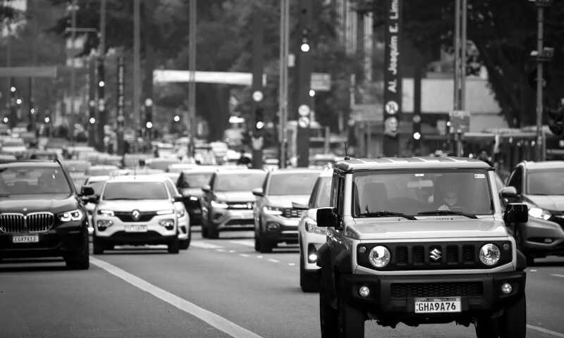 Dichter Stadtverkehr auf mehrspuriger Straße in Schwarzweiß, mit einem Suzuki Jimny im Vordergrund und weiteren PKW im Hintergrund.