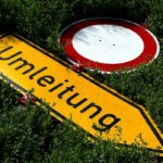 Gelbes Umleitungsschild und ein Durchfahrt-verboten-Schild liegen umgekippt im Gebüsch.