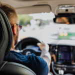 Person am Steuer eines Autos im Stadtverkehr, gesehen vom Rücksitz.