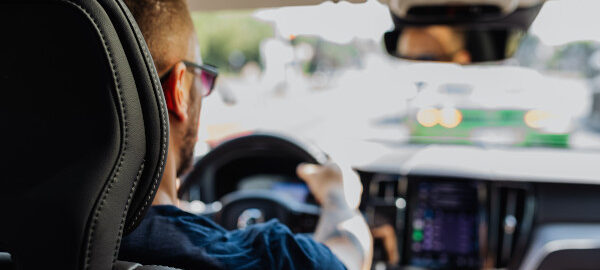 Person am Steuer eines Autos im Stadtverkehr, gesehen vom Rücksitz.